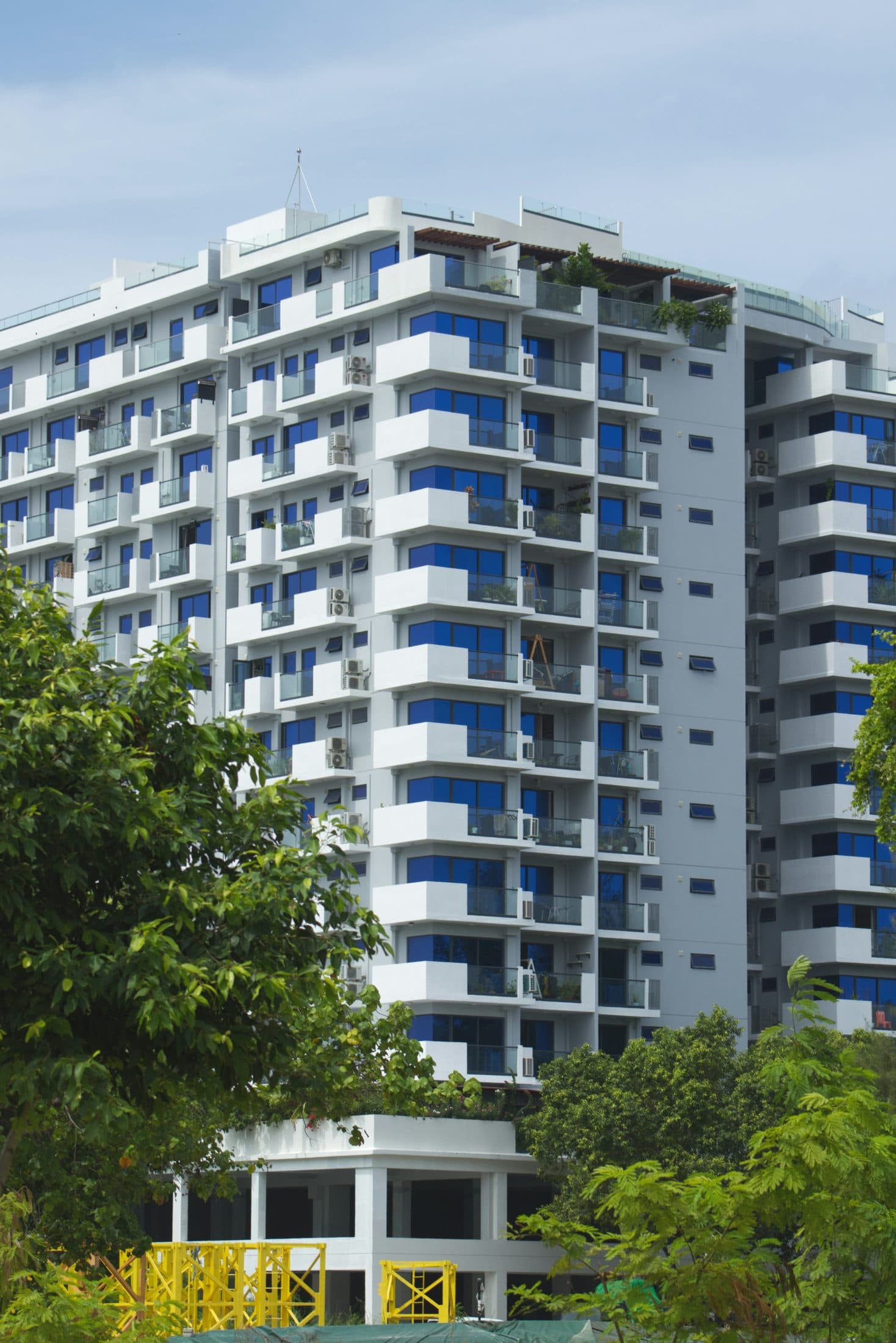 Demo image. White residential tower with blue balconies behind trees.
